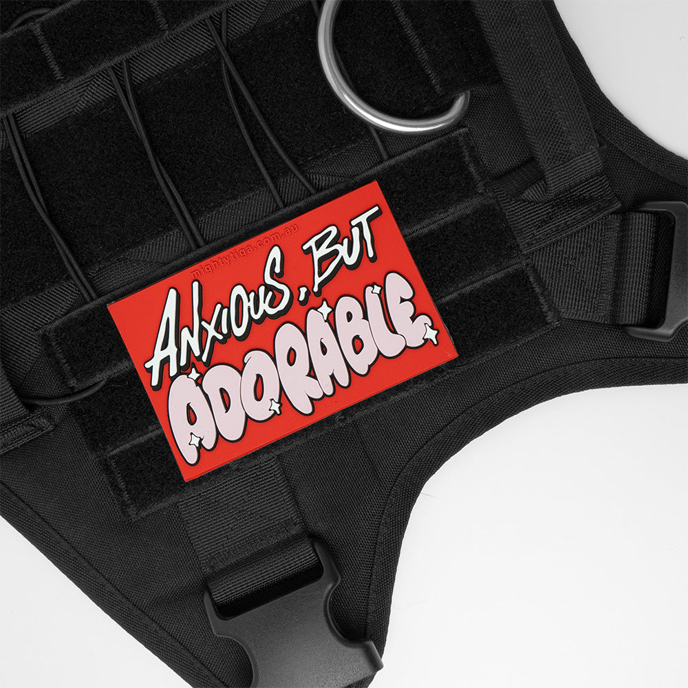 Black harness with a red PVC patch displaying 'Anxious, But Adorable' text on a white background