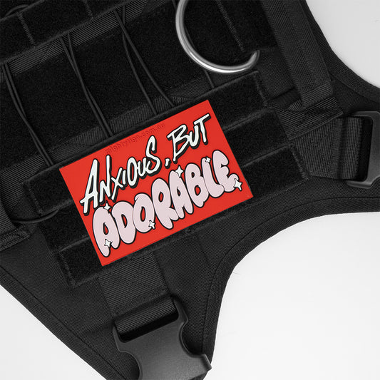 Black harness with a red PVC patch displaying 'Anxious, But Adorable' text on a white background