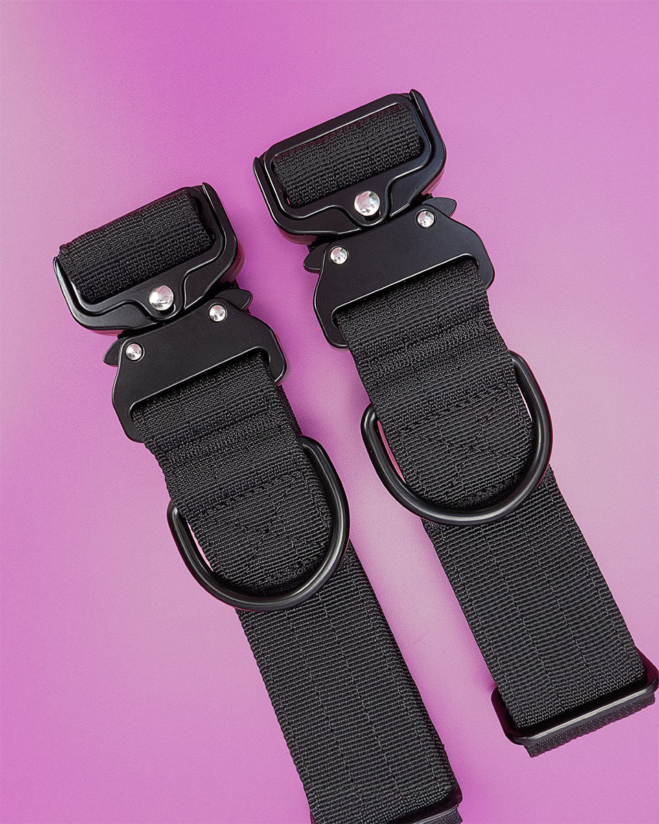 Pair of black tactical dog collars for medium and large dogs, displayed on vibrant pink background