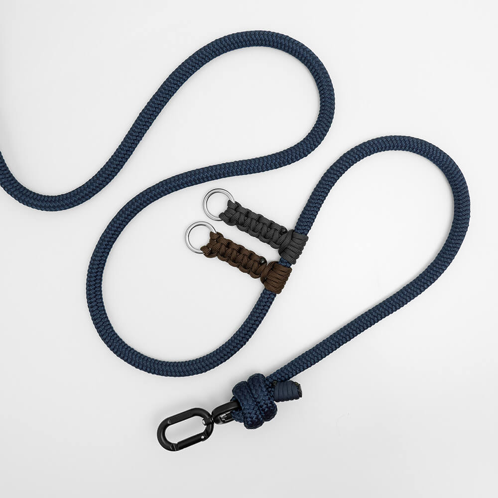 A navy blue braided rope leash with a black carabiner clip, a knotted end, and two paracord-wrapped handle sections in brown and dark gray with metal key rings, displayed on a clean white background.