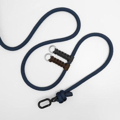 A navy blue braided rope leash with a black carabiner clip, a knotted end, and two paracord-wrapped handle sections in brown and dark gray with metal key rings, displayed on a clean white background.