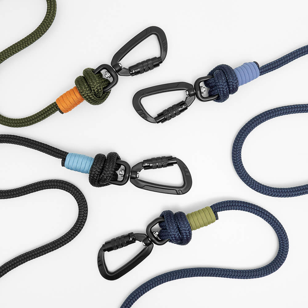Four carabiner clips attached to braided rope dog leads in different colors, arranged on a clean white background. The rope colors include army green, black, navy blue, with accent wraps in orange, light blue, lavender, and moss green.